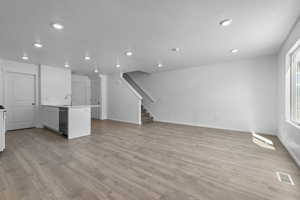 Unfurnished living room with visible vents, a sink, light wood-style flooring, and stairs