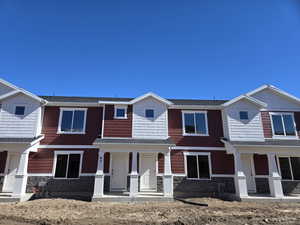 Townhome / multi-family property with a shingled roof, stone siding, and covered porch