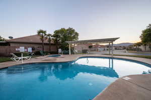 Pool at dusk featuring a pergola, a patio area, fence, and a hot tub