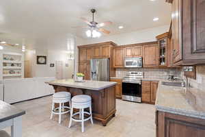 Kitchen with ceiling fan, stainless steel appliances, a sink, brown cabinets, and light stone countertops