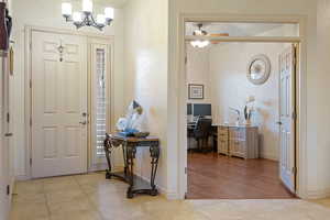 Foyer entrance featuring ceiling fan with notable chandelier, baseboards, and light tile patterned floors