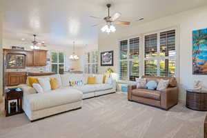 Living area with light carpet, ceiling fan with notable chandelier, visible vents, and baseboards