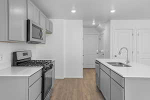 Kitchen featuring gray cabinetry, a sink, light wood-style floors, light countertops, and appliances with stainless steel finishes