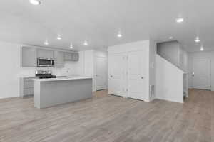 Kitchen with light wood finished floors, stainless steel appliances, light countertops, gray cabinetry, and a kitchen island with sink