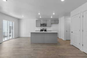 Kitchen with a kitchen island with sink, stainless steel appliances, a sink, light wood-style floors, and gray cabinets