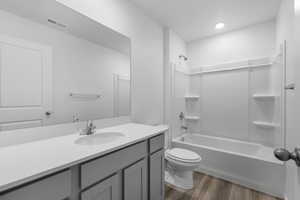 Full bathroom with visible vents, toilet, wood finished floors, vanity, and shower / washtub combination