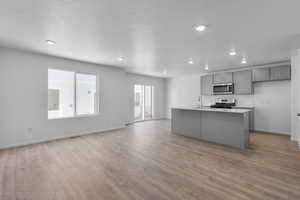 Kitchen with light wood finished floors, appliances with stainless steel finishes, gray cabinets, light countertops, and a sink