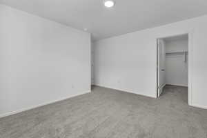 Unfurnished bedroom with a closet, baseboards, a walk in closet, and carpet flooring