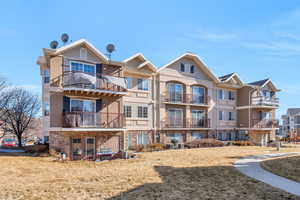 Back of property featuring a balcony, stone siding, and a yard