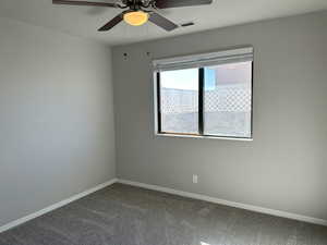 Empty room with a ceiling fan, dark carpet, visible vents, and baseboards