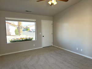 Carpeted empty room with lofted ceiling, baseboards, visible vents, and ceiling fan