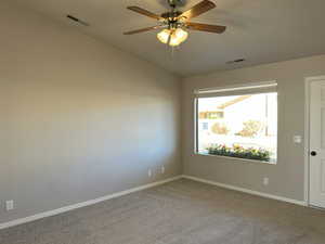 Carpeted spare room featuring a ceiling fan, visible vents, vaulted ceiling, and baseboards