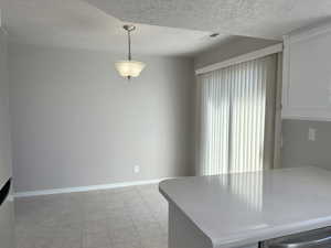 Unfurnished dining area with a textured ceiling, light tile patterned floors, visible vents, and baseboards