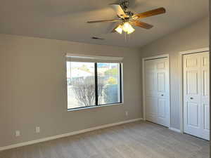 Unfurnished bedroom featuring lofted ceiling, light colored carpet, visible vents, baseboards, and multiple closets