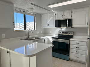 Kitchen with light countertops, appliances with stainless steel finishes, white cabinets, a sink, and a peninsula