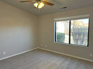 Carpeted spare room with ceiling fan, visible vents, and baseboards