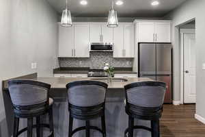 Kitchen with stainless steel appliances, a breakfast bar area, decorative backsplash, and white cabinets