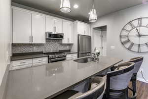 Kitchen with white cabinetry, appliances with stainless steel finishes, decorative backsplash, dark wood-style floors, and pendant lighting