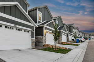 View of property exterior featuring an attached garage, concrete driveway, stone siding, a residential view, and board and batten siding