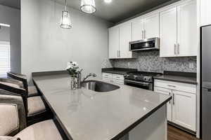 Kitchen with a breakfast bar, stainless steel appliances, hanging light fixtures, white cabinets, and a sink