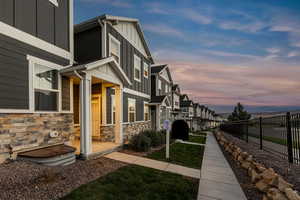 Property exterior at dusk featuring stone siding, board and batten siding, fence, and a residential view