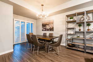 Dining room featuring dark wood-style floors, baseboards, and a notable chandelier