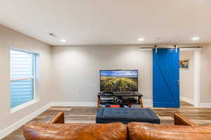 Living area featuring recessed lighting, visible vents, a barn door, wood finished floors, and baseboards