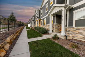 Property exterior at dusk with stone siding, a lawn, fence, and board and batten siding