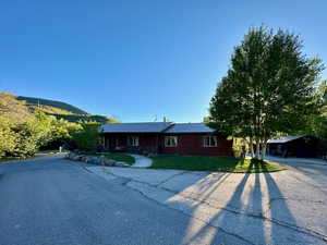 Ranch-style house with a front yard, metal roof, a mountain view, faux log siding, and driveway