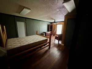 Bedroom with a textured ceiling, ceiling fan, wooden walls, wood finished floors, and ornamental molding