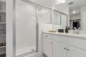 Full bath featuring a spacious closet, vanity, a shower stall, and visible vents