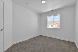 Empty room with dark colored carpet, visible vents, a textured ceiling, and baseboards