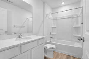 Full bath with toilet, wood finished floors, vanity, visible vents, and tub / shower combination