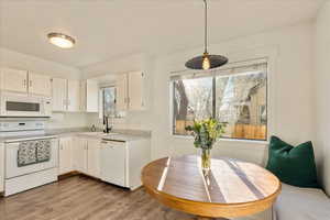 Kitchen featuring white appliances, a sink, white cabinets, light countertops, and light wood-type flooring