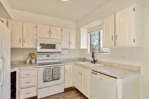 Kitchen with white appliances, white cabinets, wood finished floors, light countertops, and a sink