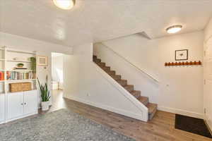 Stairway with a textured ceiling, baseboards, and wood finished floors