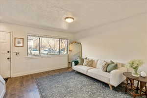 Living room with visible vents, a textured ceiling, baseboards, and wood finished floors