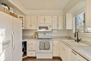 Kitchen with light countertops, white cabinets, a sink, wood finished floors, and white appliances