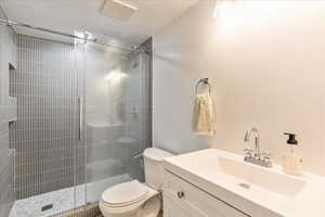 Bathroom featuring a stall shower, visible vents, toilet, a textured ceiling, and vanity