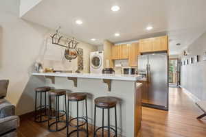 Kitchen featuring stainless steel refrigerator with ice dispenser, light countertops, light brown cabinets, washer / dryer, and a kitchen breakfast bar