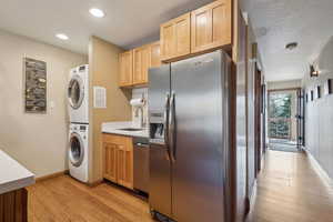 Kitchen featuring stainless steel appliances, stacked washer and dryer, light countertops, a sink, and light wood-type flooring