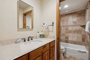 Bathroom with toilet, stone finish flooring, bathtub / shower combination, and vanity