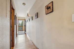 Hallway featuring light wood-style floors, a textured wall, and baseboards