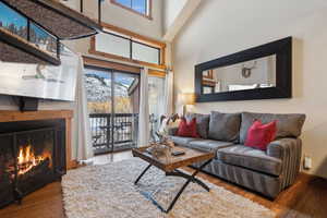 Living room featuring a towering ceiling, a lit fireplace, baseboards, and wood finished floors