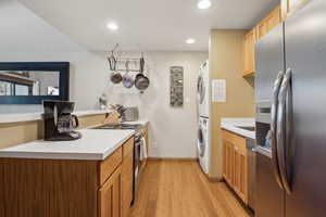 Kitchen with recessed lighting, light countertops, appliances with stainless steel finishes, stacked washing maching and dryer, and light wood-type flooring