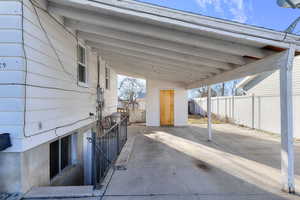 View of patio / terrace with an attached carport, an outdoor structure, fence, concrete driveway, and a storage unit