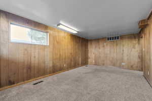 Unfurnished room with wood walls, baseboards, visible vents, and carpet flooring