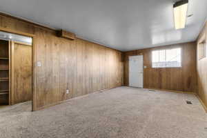 Unfurnished room featuring carpet floors, visible vents, and wooden walls