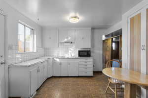 Kitchen with tasteful backsplash, black microwave, white cabinets, and a sink