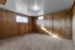 Carpeted empty room featuring visible vents, wooden walls, and baseboards